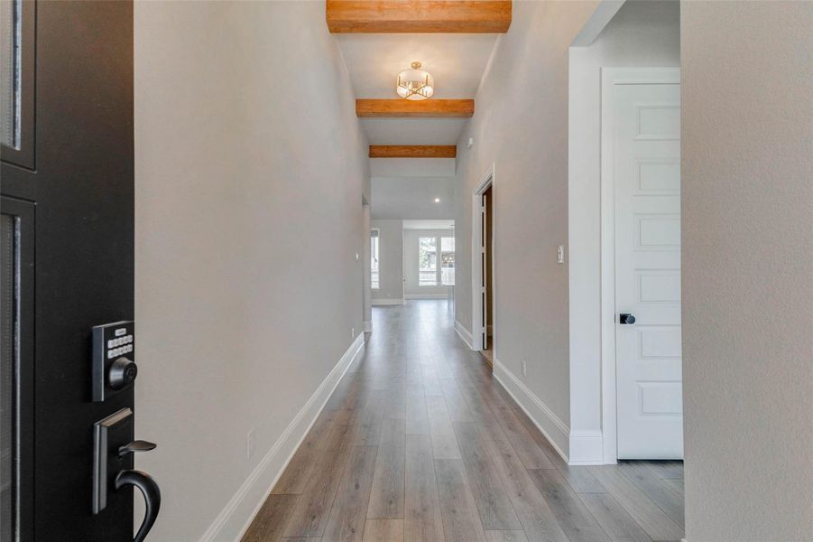 Welcoming entryway with high ceilings and wood beams. The space features neutral walls and a modern light fixture.