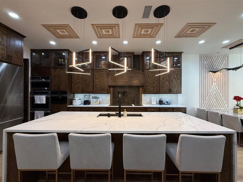 Kitchen featuring a breakfast bar area, light stone counters, backsplash, glass insert cabinets, and recessed lighting