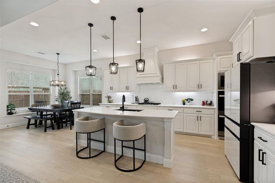 Open-concept kitchen and dining area featuring a central island, white cabinetry with dark hardware, recessed lighting, and light wood-finish flooring