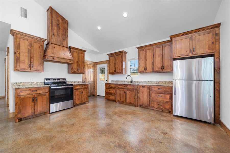 Kitchen featuring a sink, brown cabinets, custom exhaust hood, stainless steel appliances, and visible vents Kitchen featuring a sink, brown cabinets, custom exhaust hood, stainless steel appliances, and visible vents