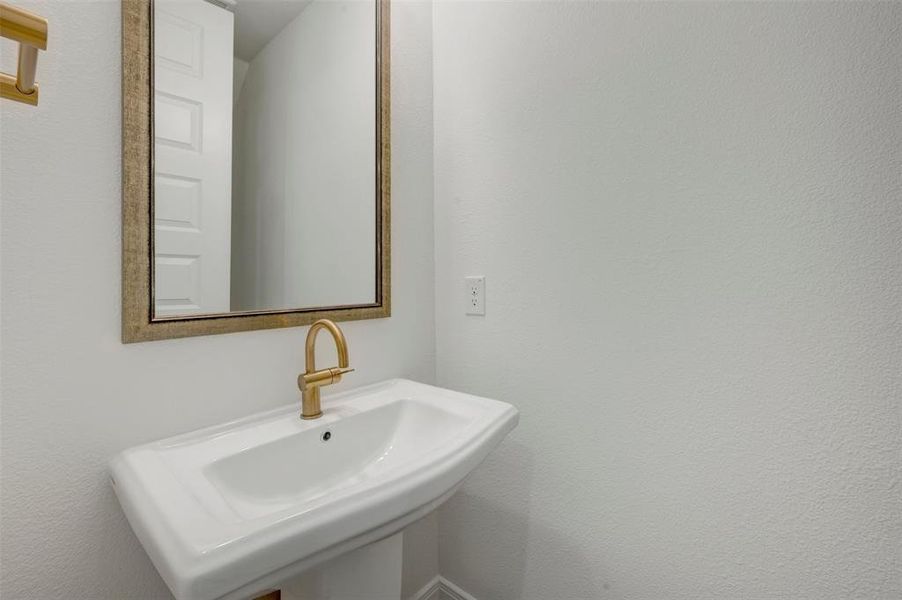 Pedestal sink featuring a single-hole gold-finish faucet, a rectangular mirror with a textured frame, and white walls