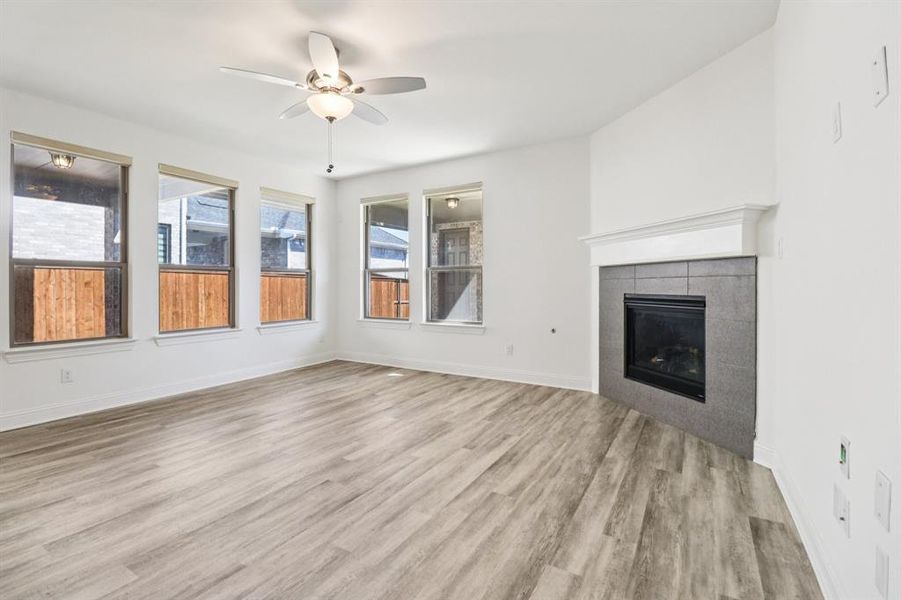 Unfurnished living room featuring light wood-style flooring, a tile fireplace, and ceiling fan Unfurnished living room featuring light wood-style flooring, a tile fireplace, and ceiling fan
