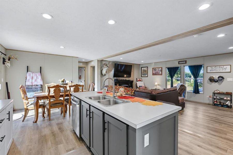 Kitchen with gray cabinetry, open floor plan, light countertops, light wood-style floors, and a kitchen island with sink Kitchen with gray cabinetry, open floor plan, light countertops, light wood-style floors, and a kitchen island with sink