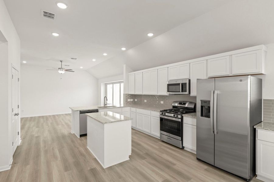 Kitchen with appliances with stainless steel finishes, white cabinets, decorative backsplash, a peninsula, and vaulted ceiling