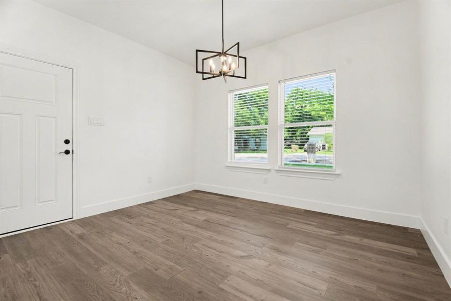 Spacious room featuring light wood flooring, white walls, two windows with blinds, and a contemporary chandelier