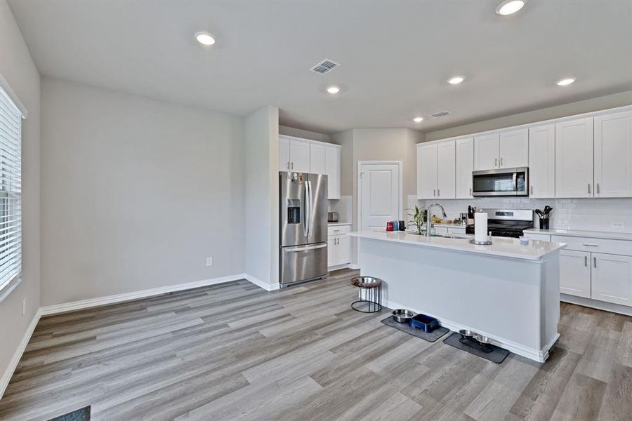 The kitchen features white cabinetry, a white subway tile backsplash, and stainless steel appliances including a refrigerator, microwave, and stove