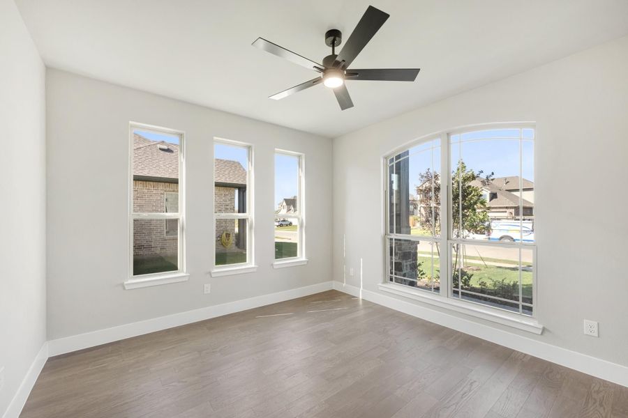 Empty room with hardwood floors, ceiling fan, and multiple large windows with neighborhood views