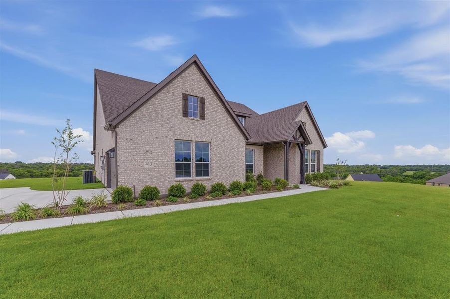Brick facade residence featuring a prominent gabled roofline, dark brown shutters, a decorative timber frame entry, a concrete driveway, and a well-maintained lawn Brick facade residence featuring a prominent gabled roofline, dark brown shutters, a decorative timber frame entry, a concrete driveway, and a well-maintained lawn