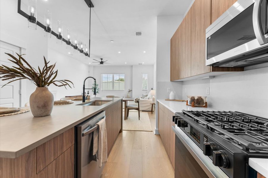 The kitchen, the heart of the second-floor open-concept living, dining, and kitchen, features a spacious island with a one-sided cascade quartz countertop, farmhouse sink, and modern pendant lights, complemented by an abundance of sleek, modern cabinetry providing ample storage, perfect for meal prep, casual breakfasts, or gathering with family and friends.