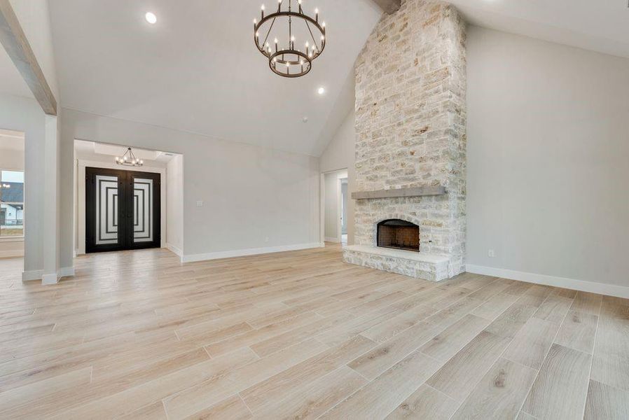 Unfurnished living room featuring a stone fireplace, light wood-type flooring, high vaulted ceiling, and an inviting chandelier