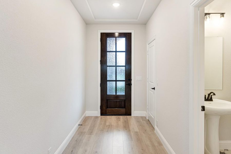 Entryway hallway with dark wood glass-panel front door, light hardwood floors, and white walls