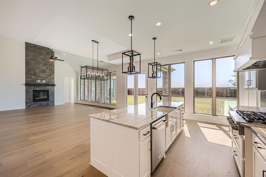 Kitchen with stainless steel appliances, light stone countertops, white cabinets, a tile fireplace, and light hardwood / wood-style flooring