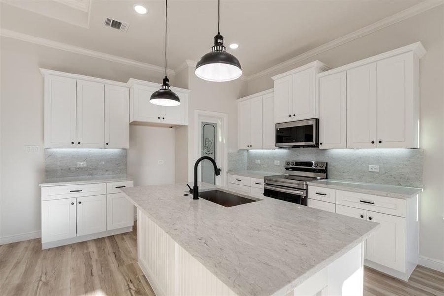 Kitchen with appliances with stainless steel finishes, white cabinets, light stone counters, backsplash, and ornamental molding