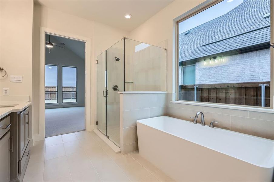 Bathroom with ceiling fan, tile patterned floors, vaulted ceiling, shower with separate bathtub, and vanity