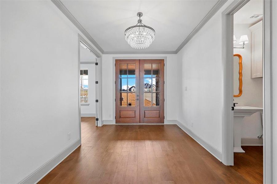 Entryway featuring dark hardwood / wood-style flooring, crown molding, french doors, and an inviting chandelier