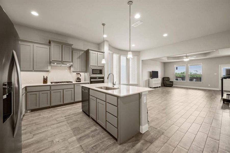 Open view of the gourmet kitchen flowing into the living area, complete with upgraded cabinetry, stainless steel appliances, and plenty of natural light from surrounding windows.