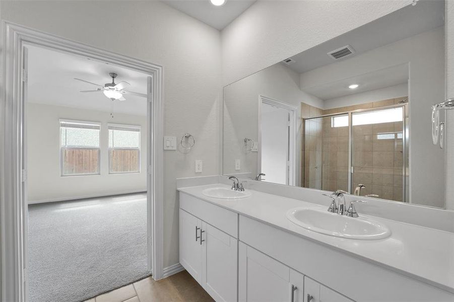 Full bath with a shower stall, double vanity, light tile patterned floors, and ceiling fan Full bath with a shower stall, double vanity, light tile patterned floors, and ceiling fan