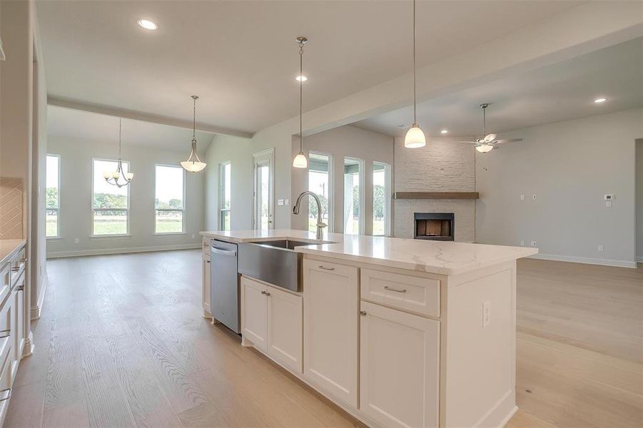 Kitchen with an island with sink, white cabinetry, light hardwood / wood-style floors, dishwasher, and a fireplace