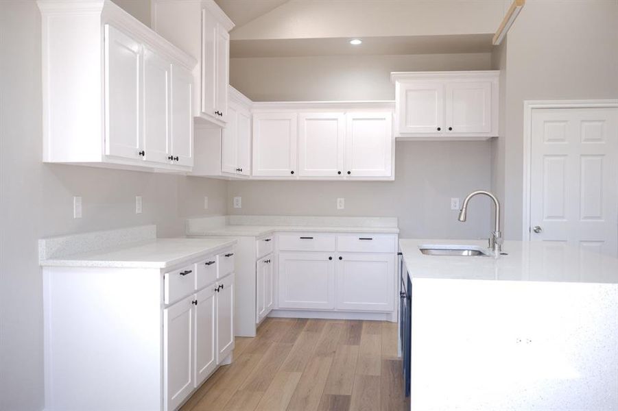 Kitchen with white cabinets, light stone counters, light wood-type flooring, vaulted ceiling, and a center island with sink Kitchen with white cabinets, light stone counters, light wood-type flooring, vaulted ceiling, and a center island with sink