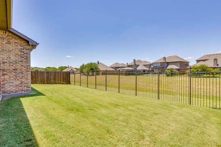 Expansive grassy yard area featuring a brick exterior, a wood privacy fence, and a black wrought iron fence