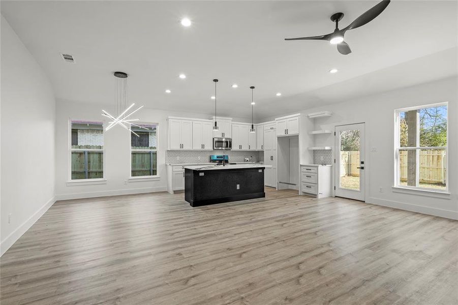 Kitchen with stainless steel appliances, white cabinets, an island with sink, and hanging light fixtures