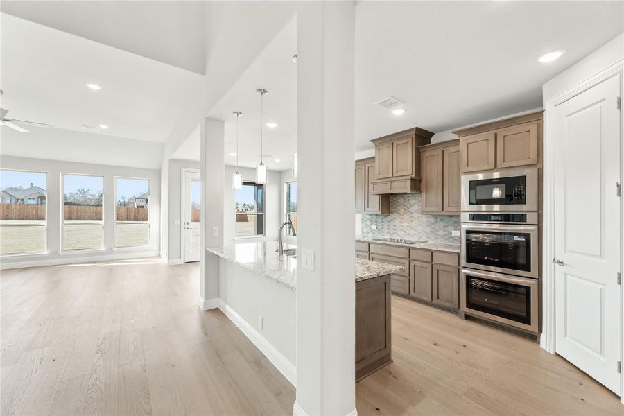 Open-concept kitchen with tan cabinets, stainless steel appliances, granite island, and light hardwood floors flowing into living area Open-concept kitchen with tan cabinets, stainless steel appliances, granite island, and light hardwood floors flowing into living area