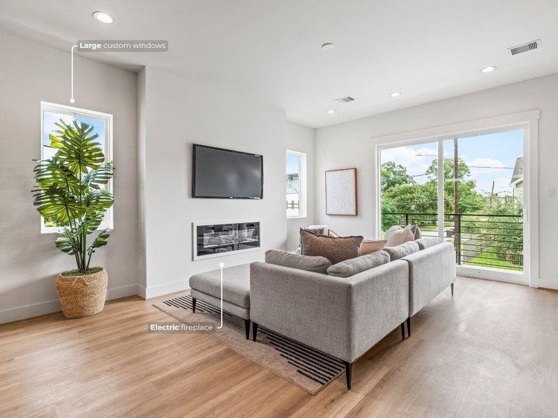 This living room has an electric fireplace for cozy nights in, custom windows that flood the space with natural light, and durable LVP flooring that runs throughout the home.