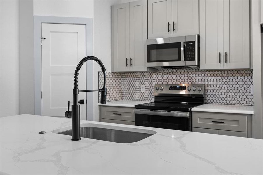 Kitchen featuring gray cabinets, stainless steel appliances, and light stone counters