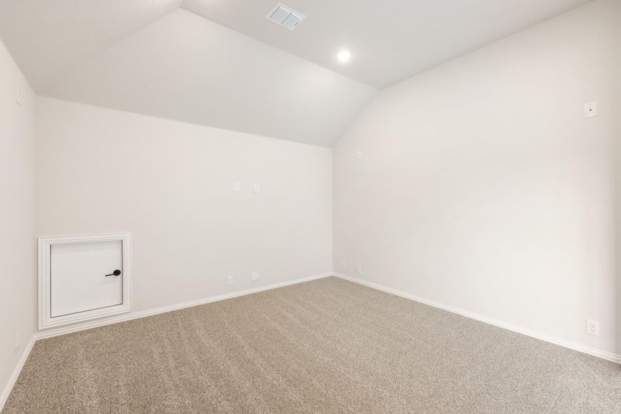 Empty room with vaulted ceiling, beige carpet, white walls, and a small access panel door. Empty room with vaulted ceiling, beige carpet, white walls, and a small access panel door.