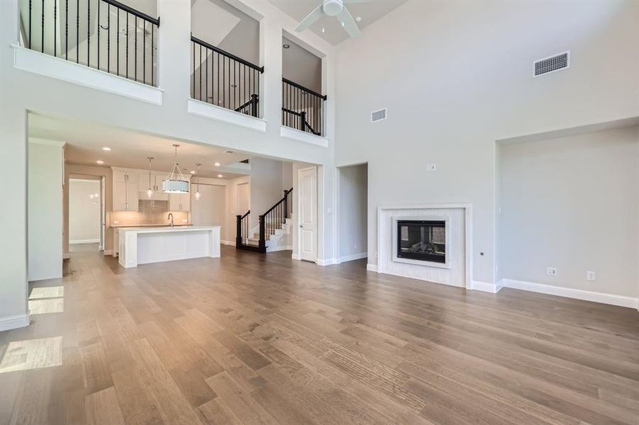 Unfurnished living room featuring ceiling fan, wood-type flooring, sink, and a high ceiling