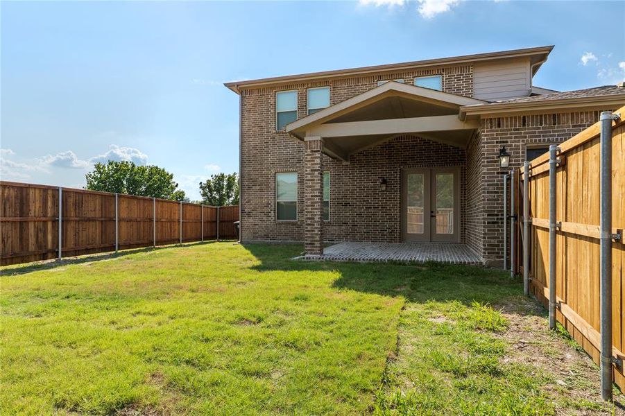 Rear view of property featuring a fenced backyard, a patio, brick siding, and french doors Rear view of property featuring a fenced backyard, a patio, brick siding, and french doors