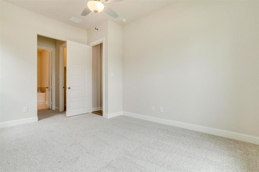 Unfurnished bedroom featuring light carpet, ensuite bath, and ceiling fan