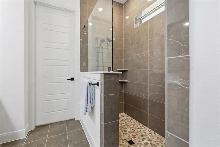 Walk-in shower featuring glass enclosure, stone tile walls, pebble flooring, and integrated shelving Walk-in shower featuring glass enclosure, stone tile walls, pebble flooring, and integrated shelving