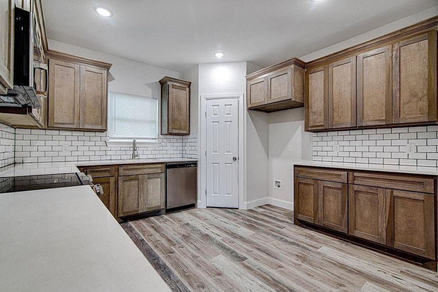 Kitchen featuring light hardwood / wood-style floors, sink, dishwasher, and tasteful backsplash