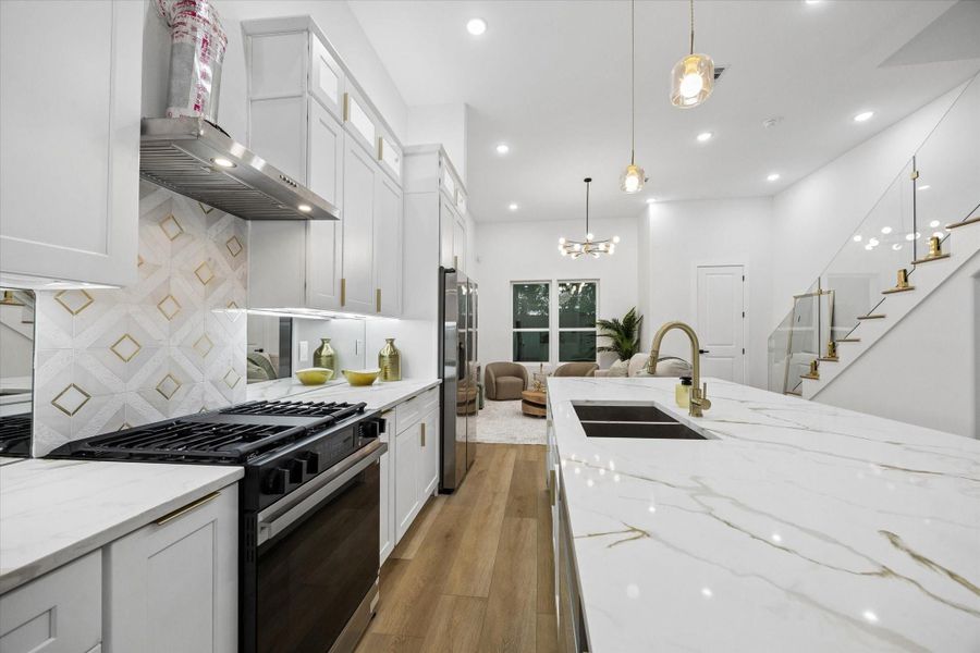 This modern home features an open-concept kitchen and living area with sleek white cabinetry, marble countertops, and a spacious island. The room is well-lit with recessed lighting, pendant lights, and a contemporary chandelier. A staircase with glass railings adds a touch of elegance, leading to the upper level. This modern home features an open-concept kitchen and living area with sleek white cabinetry, marble countertops, and a spacious island. The room is well-lit with recessed lighting, pendant lights, and a contemporary chandelier. A staircase with glass railings adds a touch of elegance, leading to the upper level.