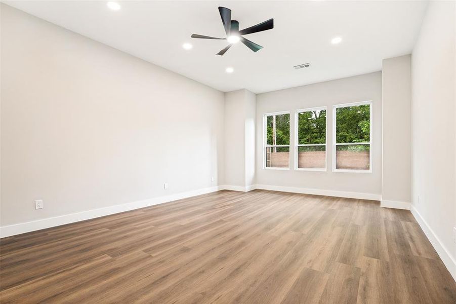 Spacious room featuring wood-finish flooring, white baseboards, and three large windows providing ample natural light