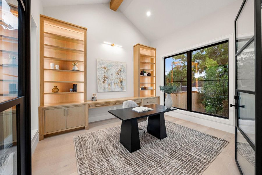A thoughtfully designed study featuring custom micro-shaker cabinetry with integrated lighting, creating both function and visual warmth . A large picture window frames views of the outdoors while bringing in natural light, making the space feel open yet grounded. Clean lines, built-in storage, and a quiet, tucked-away location make this an ideal setting for focused work or creative pursuits.
