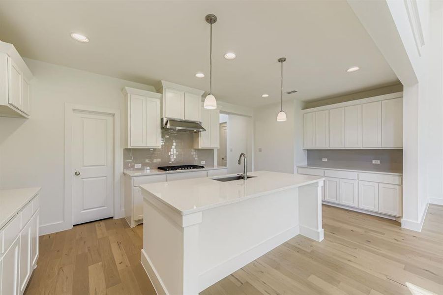 Kitchen with decorative backsplash, recessed lighting, light wood finished floors, white cabinetry, and decorative light fixtures Kitchen with decorative backsplash, recessed lighting, light wood finished floors, white cabinetry, and decorative light fixtures