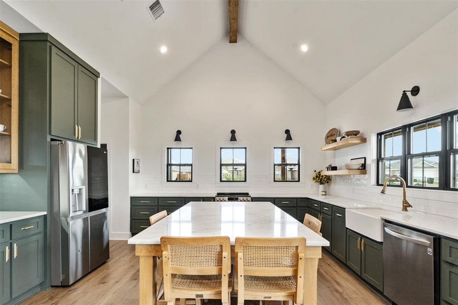 Kitchen with appliances with stainless steel finishes, open shelves, green cabinetry, beam ceiling, and backsplash