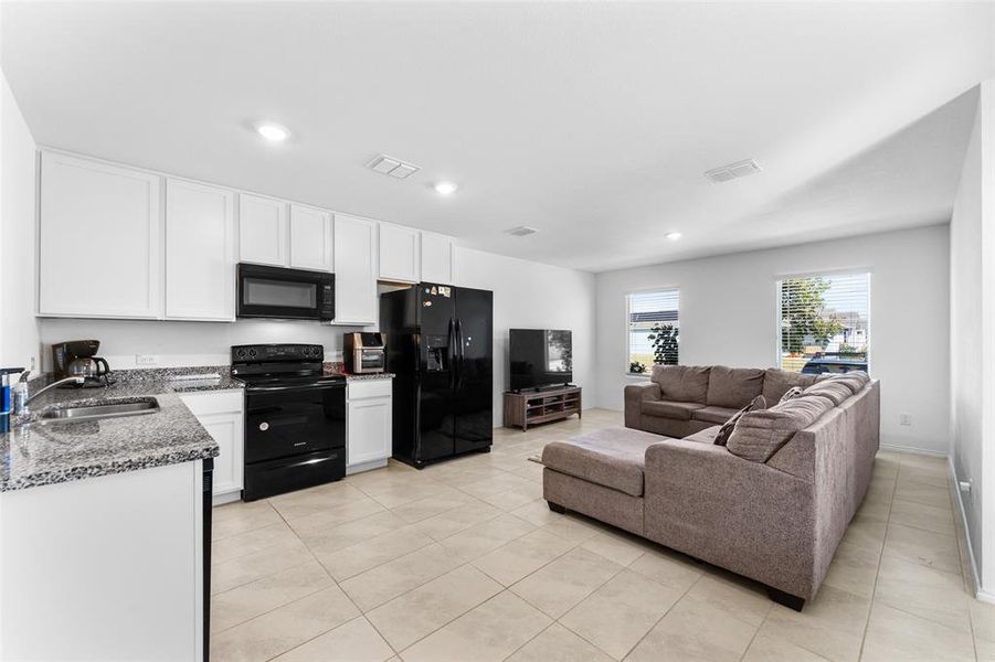 Kitchen featuring black appliances, dark stone counters, white cabinetry, light tile patterned flooring, and recessed lighting Kitchen featuring black appliances, dark stone counters, white cabinetry, light tile patterned flooring, and recessed lighting