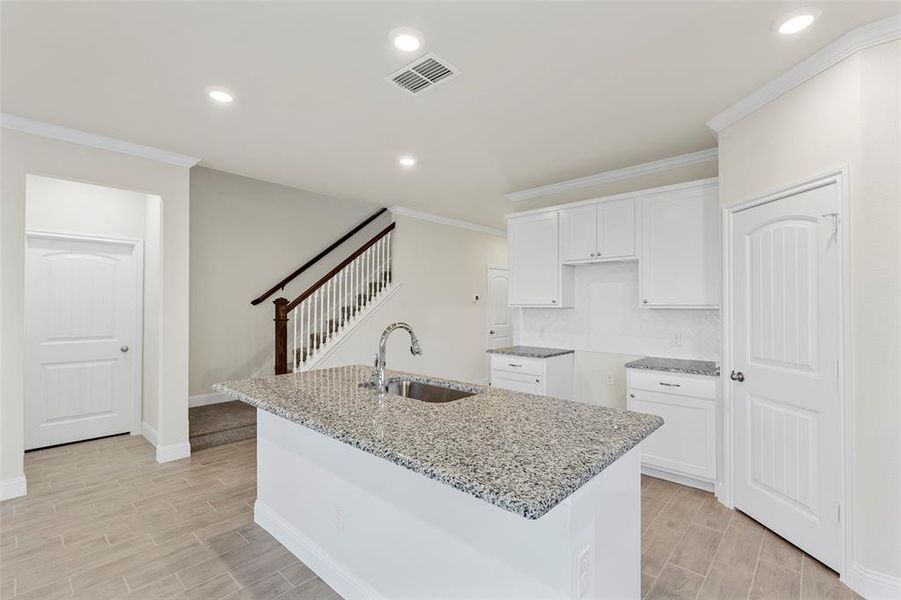 Kitchen with light stone counters, white cabinetry, a kitchen island with sink, and sink