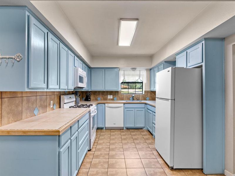 Kitchen featuring white appliances, blue cabinets, and decorative backsplash Kitchen featuring white appliances, blue cabinets, and decorative backsplash