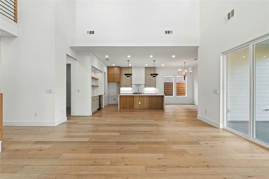 Unfurnished living room featuring light wood-type flooring, a towering ceiling, and a chandelier