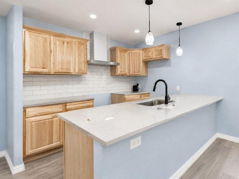 Kitchen featuring light wood cabinetry, white subway tile backsplash, light-toned countertops, and a stainless steel sink with a matte black faucet