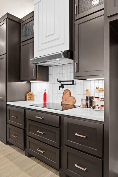 Kitchen featuring light countertops, tasteful backsplash, black electric stovetop, and under cabinet range hood Kitchen featuring light countertops, tasteful backsplash, black electric stovetop, and under cabinet range hood