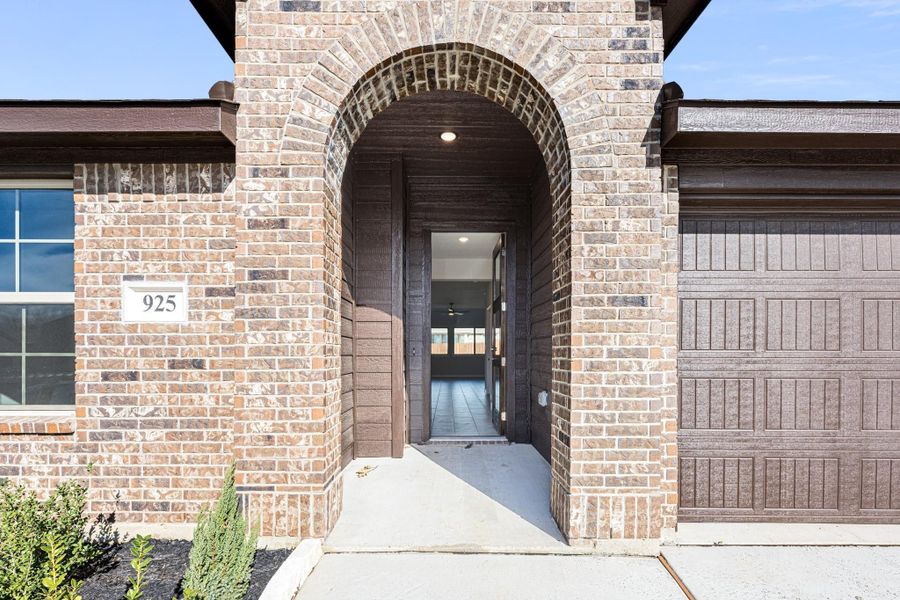 Brick home entrance with arched entryway, dark front door, and attached garage Brick home entrance with arched entryway, dark front door, and attached garage