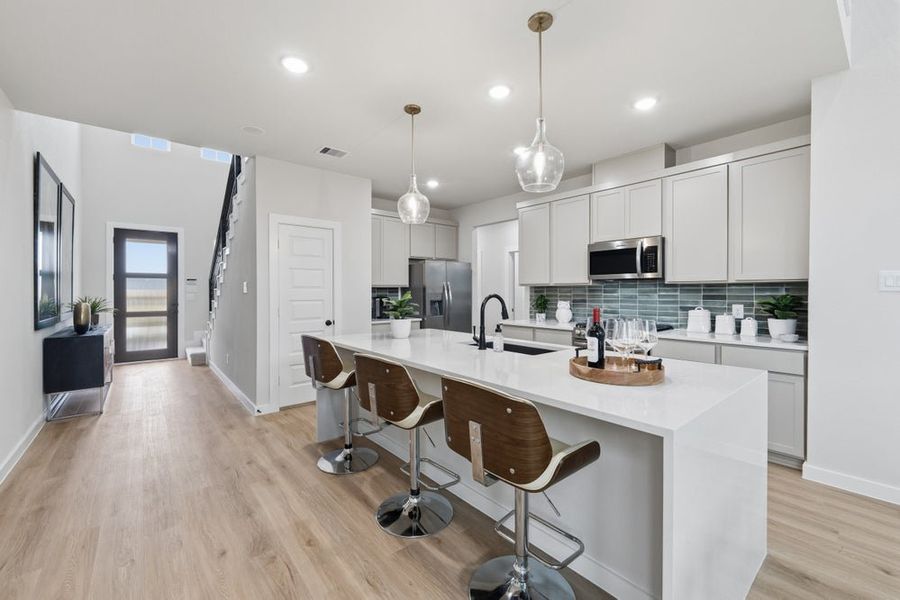 Open kitchen featuring white cabinetry, quartz island with seating, and teal tile backsplash Open kitchen featuring white cabinetry, quartz island with seating, and teal tile backsplash