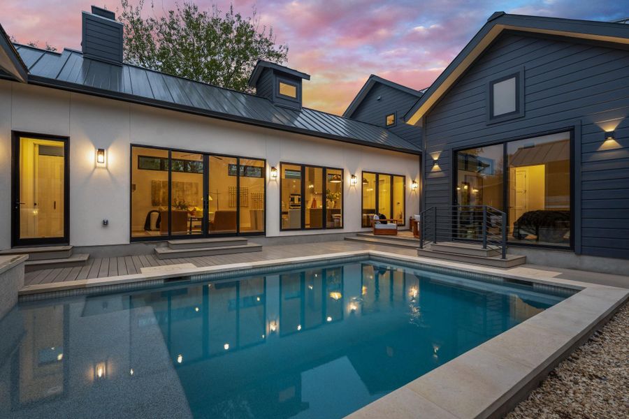 Back of property at dusk featuring an outdoor pool, a standing seam roof, a metal roof, and a patio area