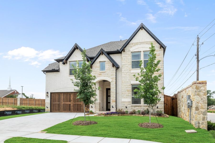 Two-story home with stone and brick exterior, dark roof, two-car garage, and landscaped front yard