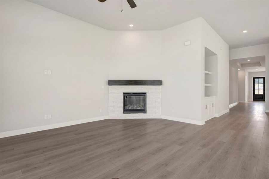 Unfurnished living room featuring a brick fireplace, built in shelves, a ceiling fan, wood finished floors, and recessed lighting